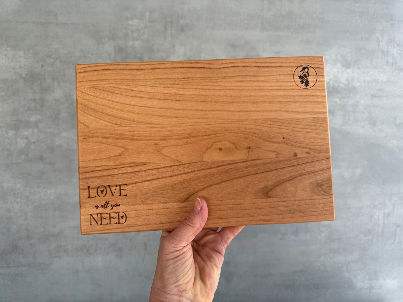 Hand hält ein Brotzeitbrett aus Kirschbaum mit Laserung für Valentinstag in die Luft.