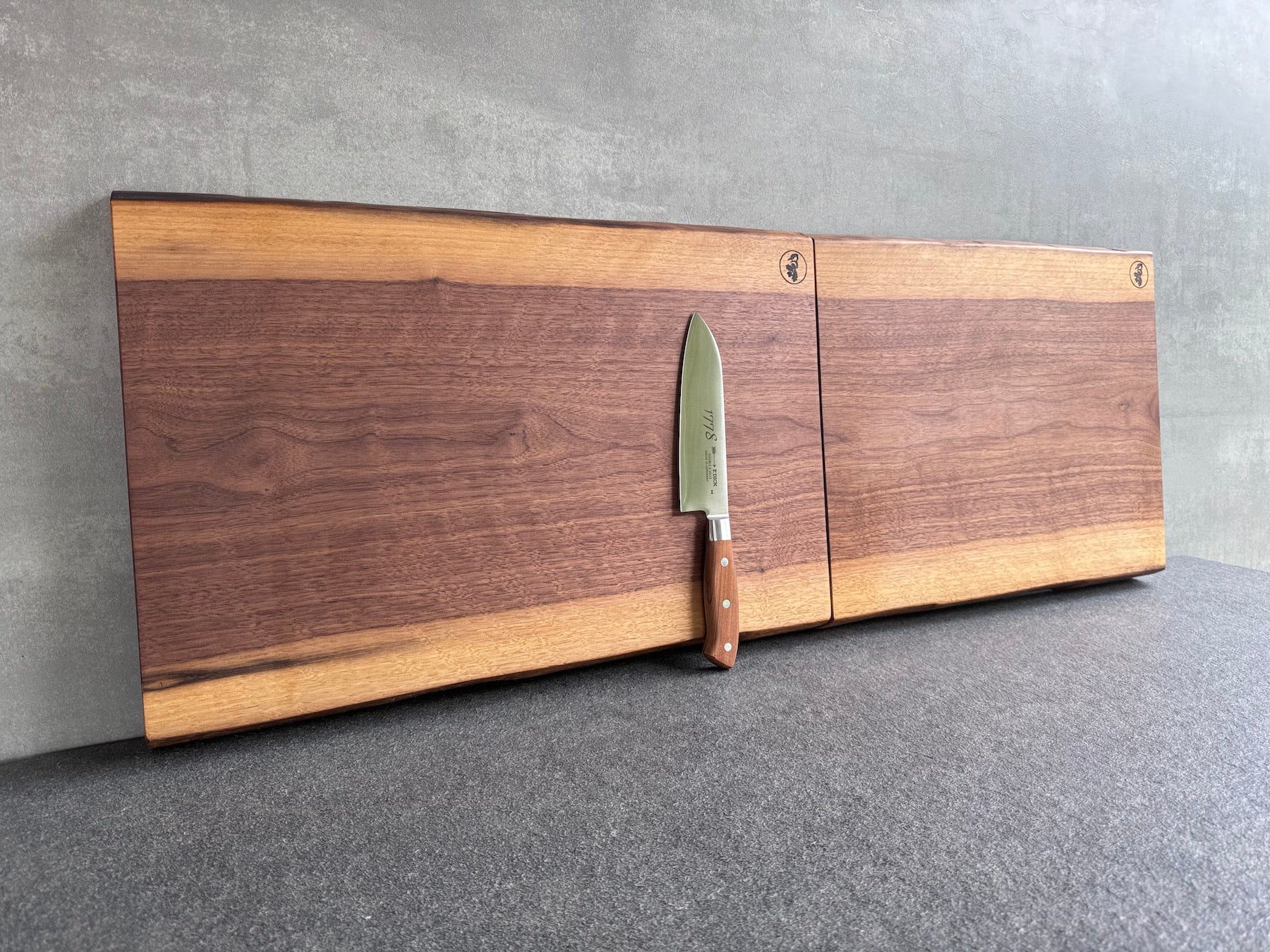 2 Nussbaum Schneideblöcke aus einer Nussbaumbohle aneinander. Insgesamt über 110 cm Länge! Mit einem Dick Santoku 1778 dekoriert.