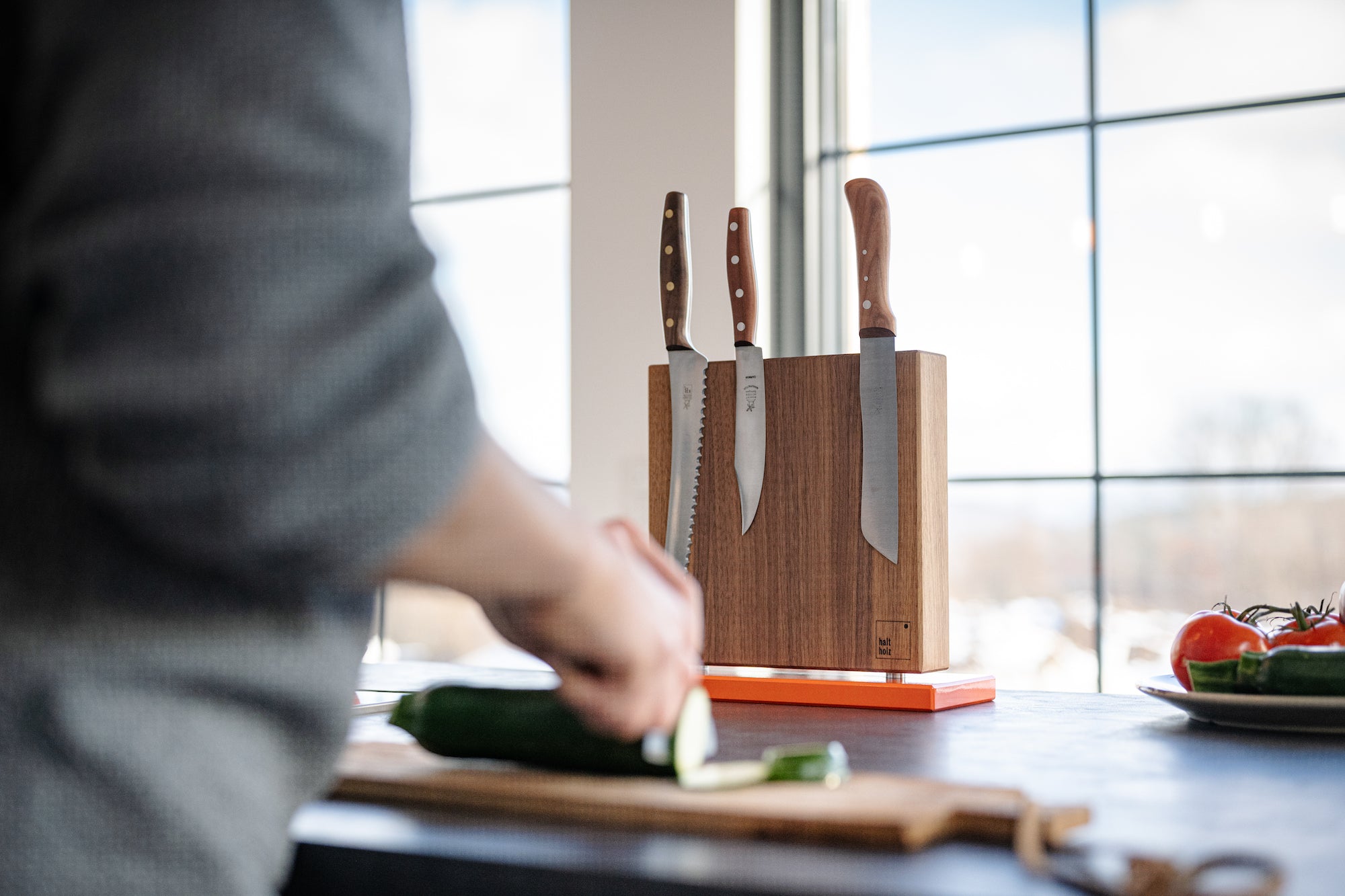 Magnetischer Messerblock für bis zu 10 Messer mit einem Stahlsockel in einer hellen Küche.  Im Vordergrund schneidet ein Koch Gemüse.
