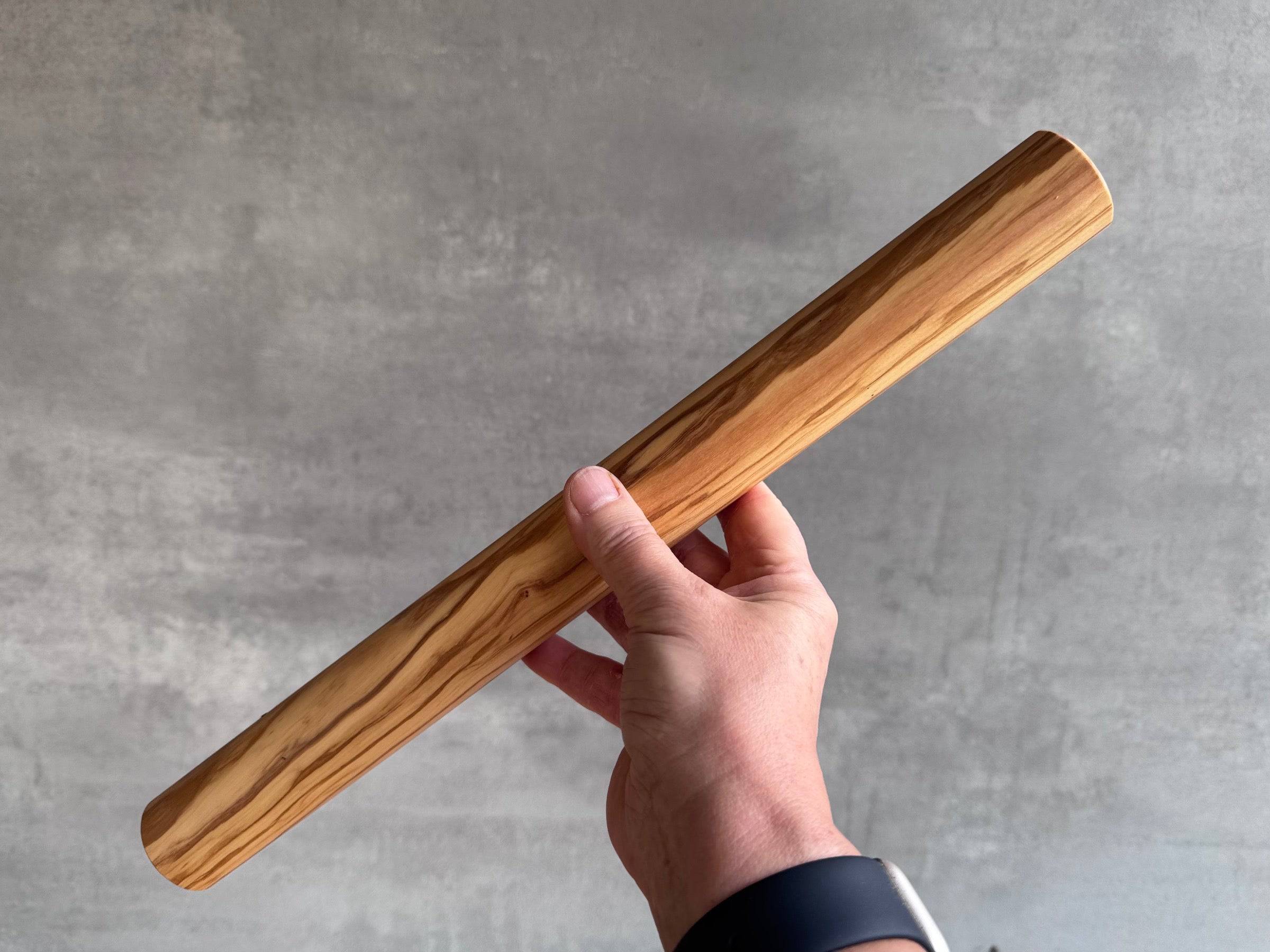 Hand hält eine 40 cm lange Teigrolle aus Olivenholz hoch.