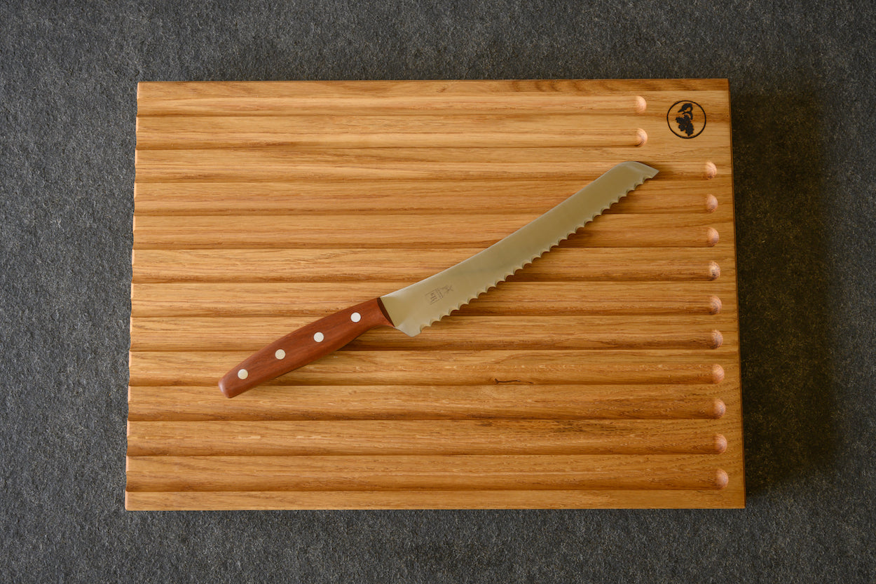 Brotmesser für Linkshänder mit einem Pflaumegriff auf einem großen Brotschneidebrett von Spessartbrett liegend.