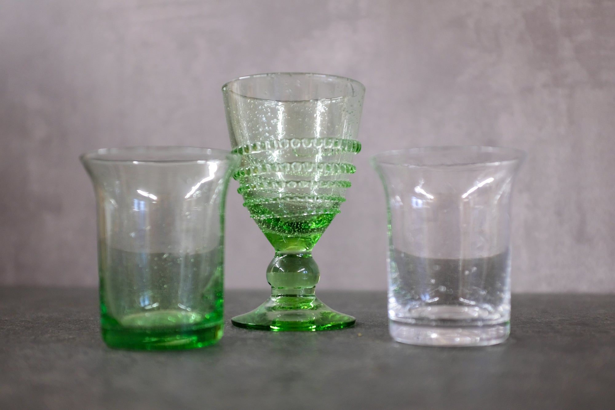 Wasserglas, Weinglas und Trinkglas  aus der Lauschaer Glaswelt in einer Reihe auf einer Steinplatte. 