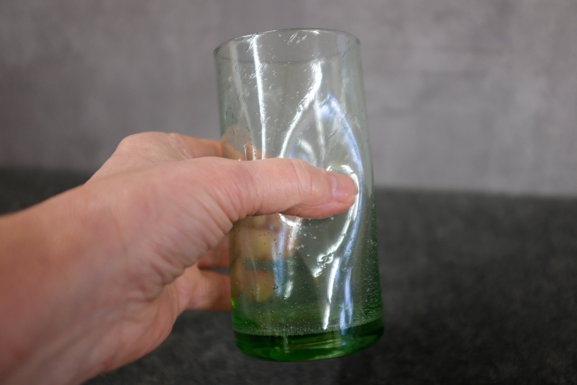 In der Hand ein grünes Trinkglas mit Griffmulden.