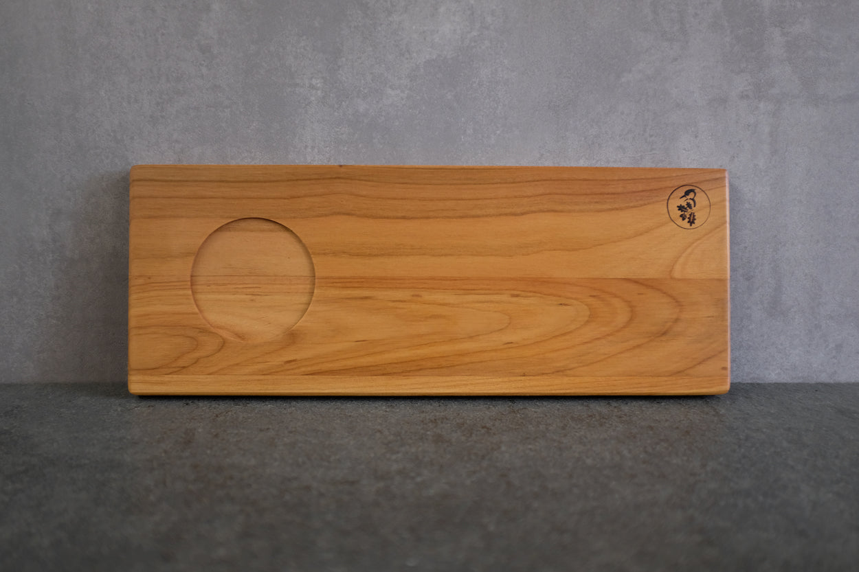 Holz Tablett aus massiver Kirsche mit einer Vertiefung für eine große Tasse an einer Betonwand angelehnt.