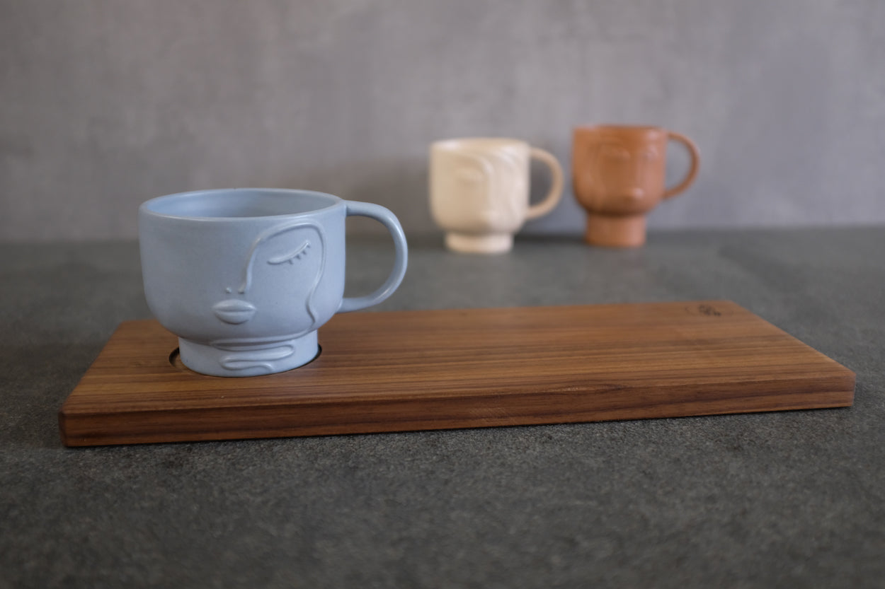 Rechteckiges Holz Tablett aus Nussbaum massiv mit einer Vertiefung für einen Becher. Dekoriert mit einer blauen  Keramik Tasse mit Gesicht.